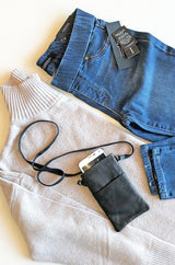 A flat lay showing a winter themed outfit knitted top and jeans paired with black cross body phone bag
