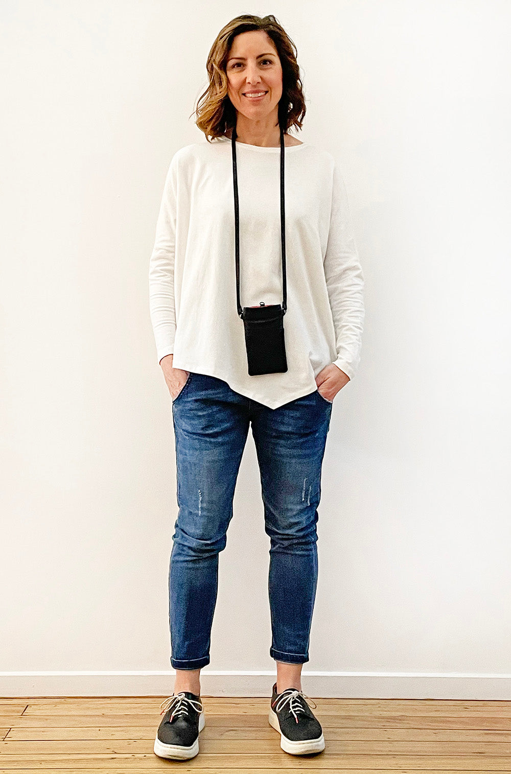 woman with white top showing her phone inside a black Leather Phone Bag