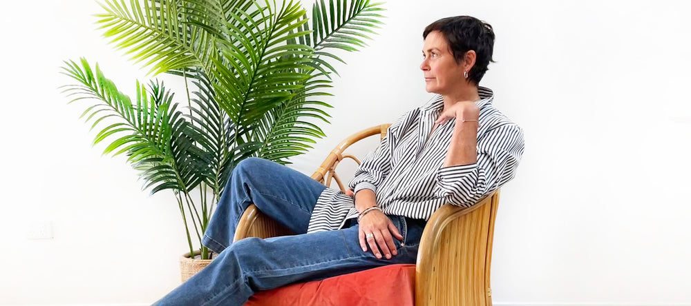 Women wearing striped shirt and jeans. She is sitting in a cane chair with a red cushion