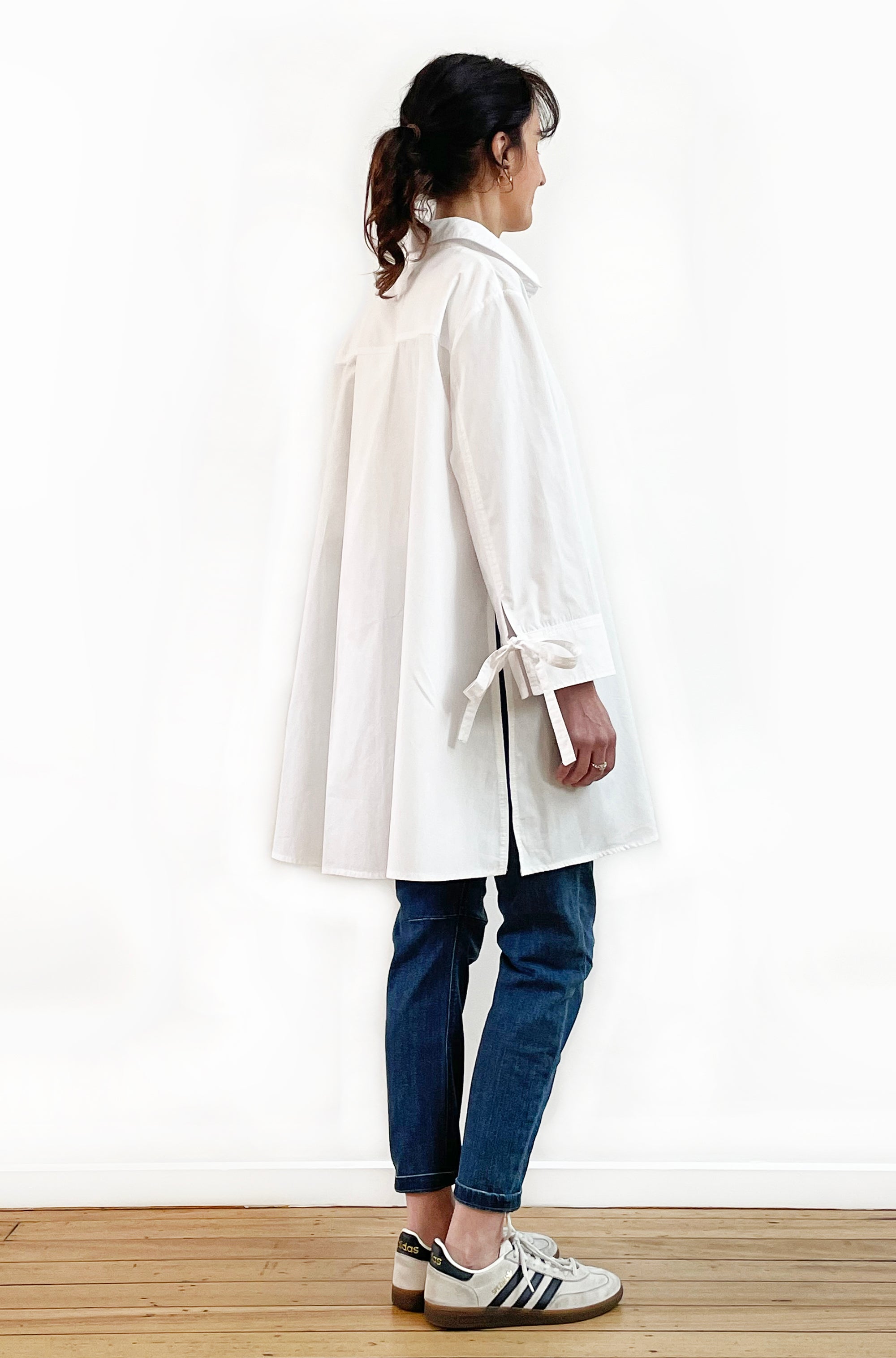 Person wearing a white shirt and blue jeans standing against a white wall.