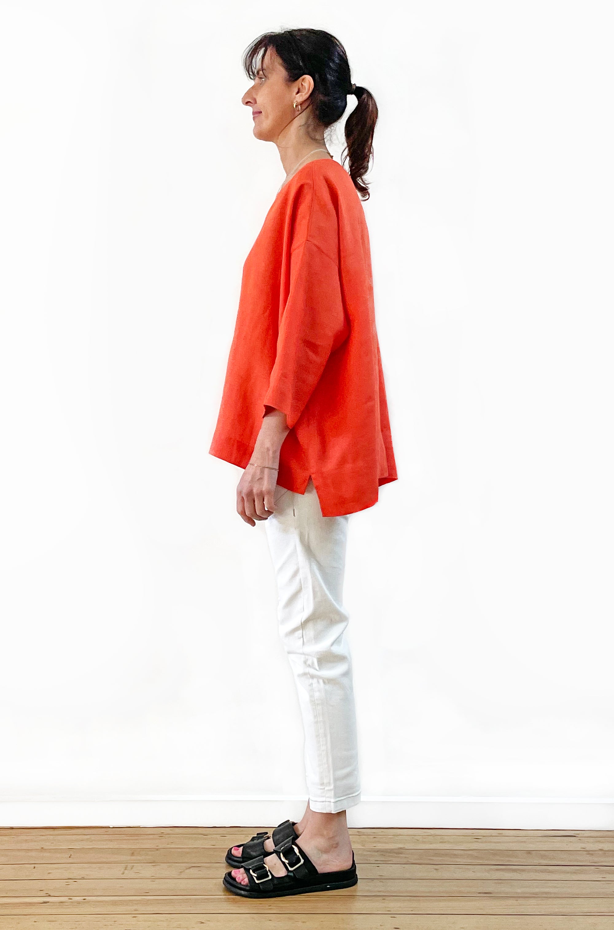 Woman wearing an orange top and white pants on a white background